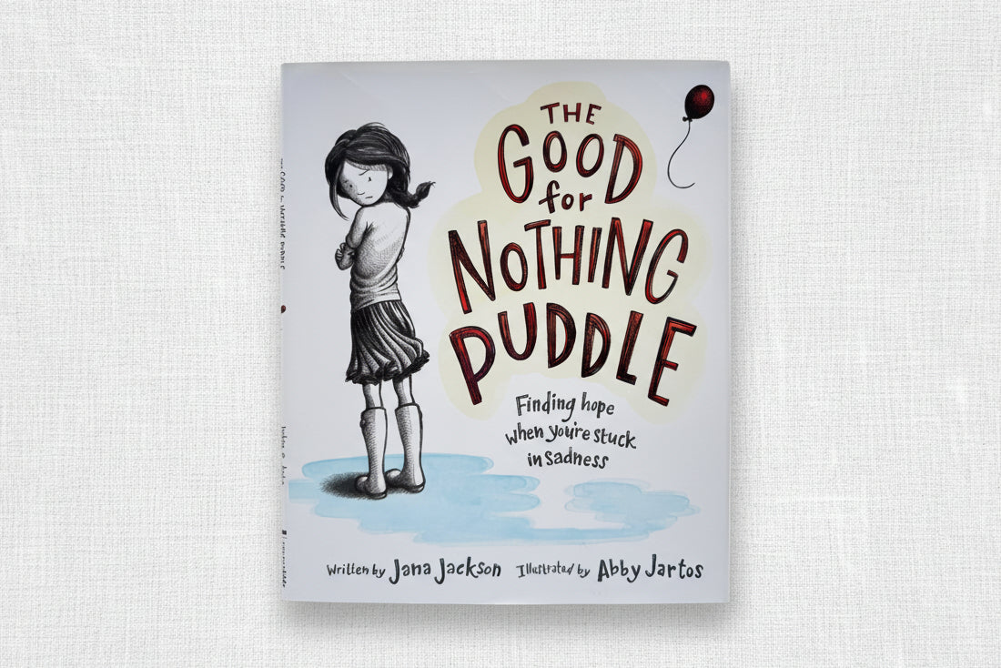 Book cover of 'The Good for Nothing Puddle' with a girl standing in a puddle.