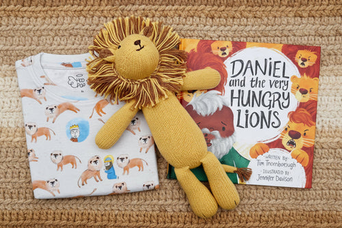 Load image 1 in gallery view. White shirt with lion pattern, knitted lion toy and a children's book titled 'Daniel and the Very Hungry Lions' on a brown background.