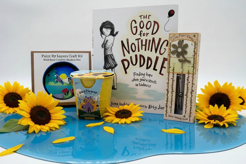 Load image 1 in gallery view. Collection of children's book, flower growing kit, wind chime and craft on tan background