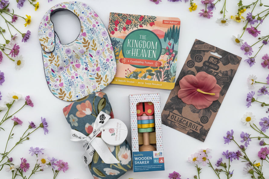 Baby bib, swaddle blanket, teether, book, and wooden toy with flowers in the background