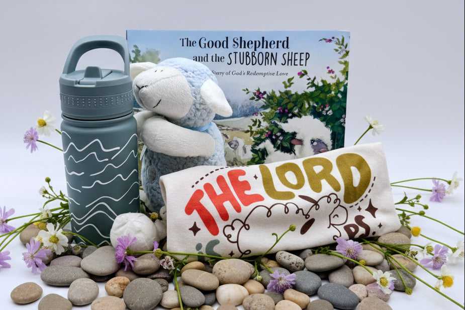 Set of children's items including a t-shirt, water bottle, plush lamb toy, and book titled 'The Good Shepherd and the Stubborn Sheep' on a cream colored background.