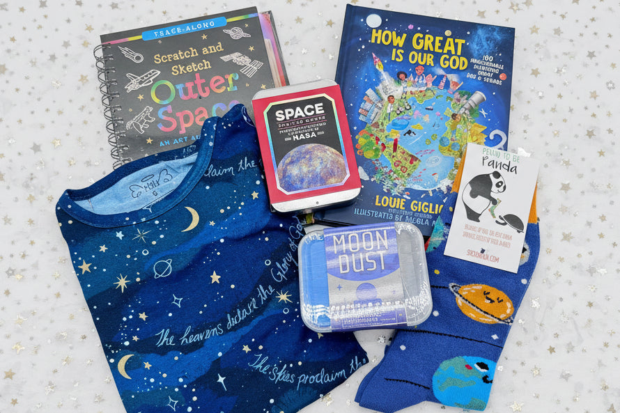 Collection of space-themed items including books, pajamas, playing cards, socks, and container of play sand 